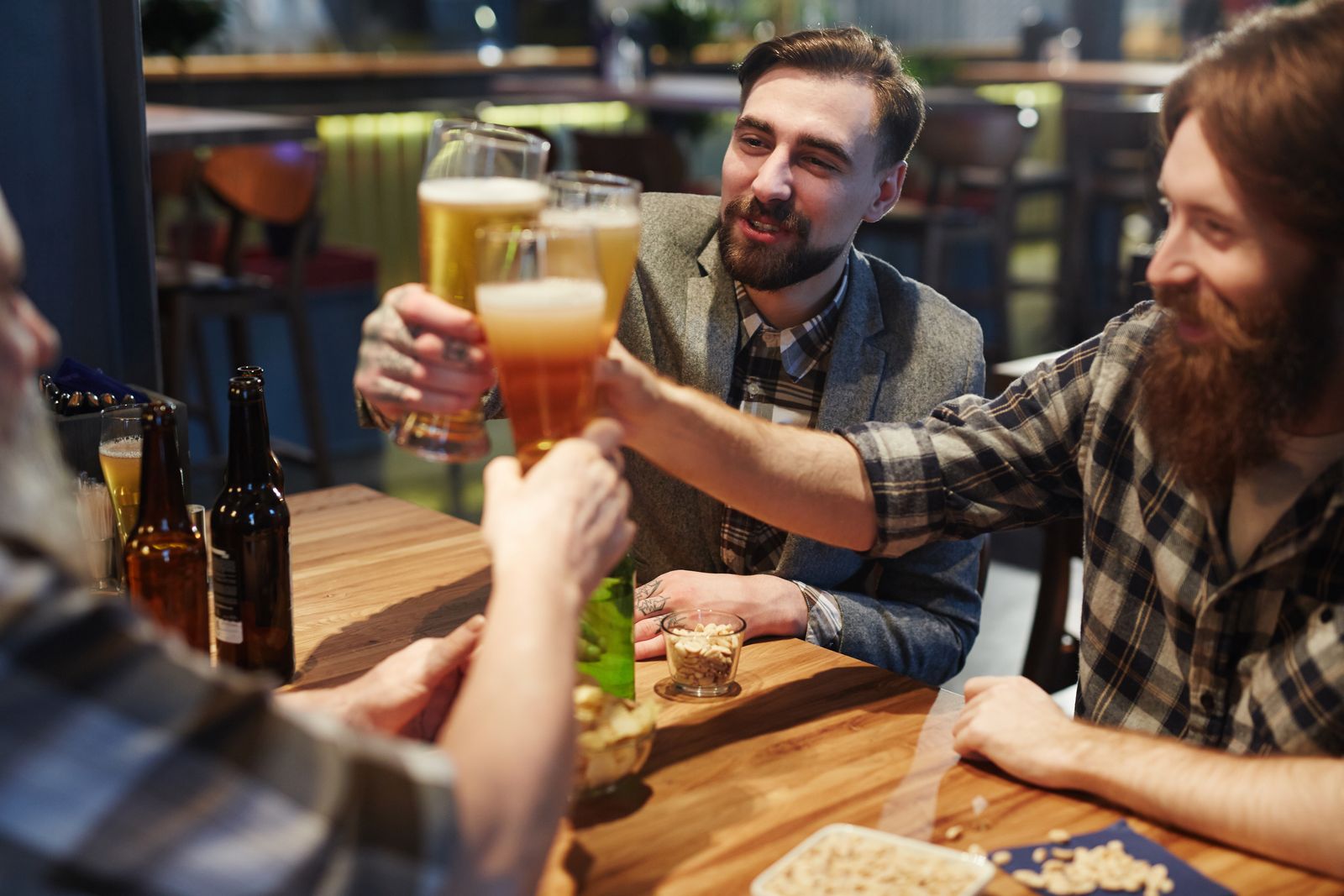 Friends in flannel shirts toasting with beers at a bar table